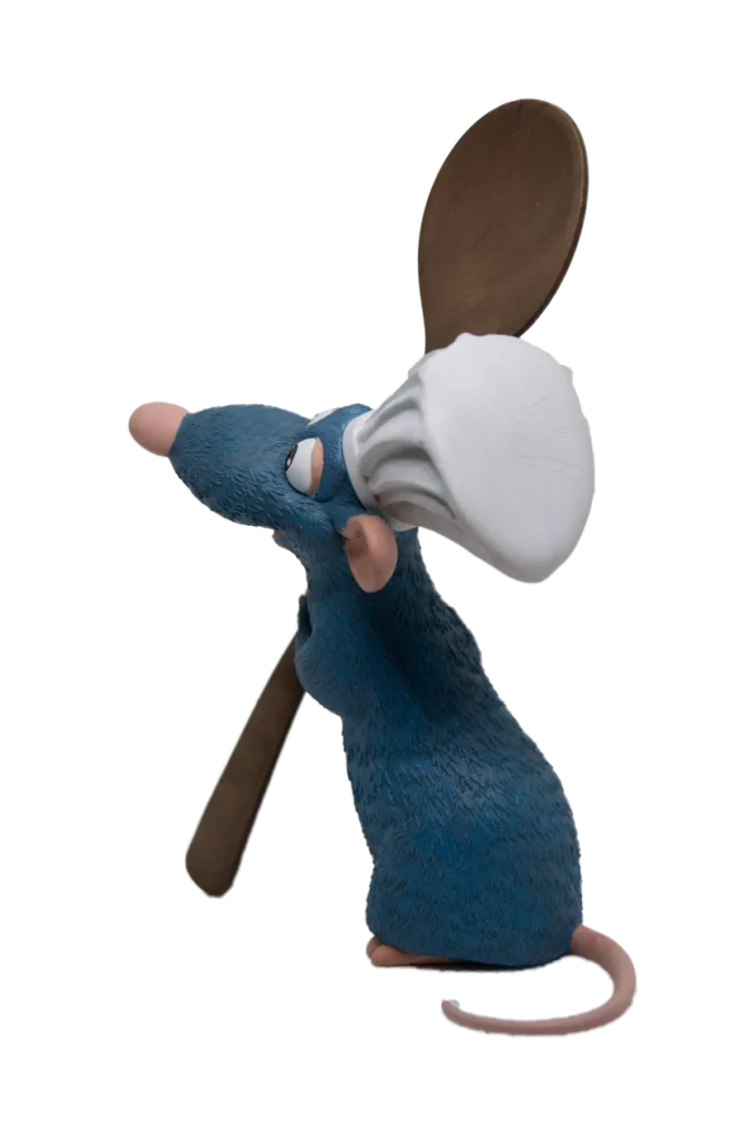 3D фигурa на Реми от „Рататуй“ в страничен изглед, усмихнат и държащ дървена лъжица, облечен с готварска шапка.